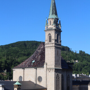 An impressive church with a tall tower rises above the city. In the background, gentle hills and a blue sky are visible.