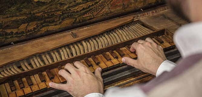 A musician plays on a historic piano. The keys are made of wood and the piano has intricate decorations. | © Flora Bacher