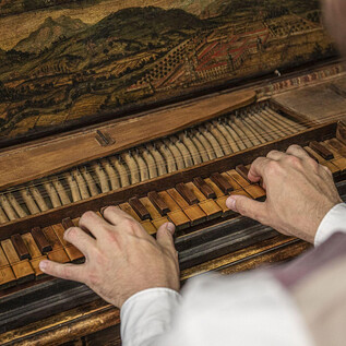 A musician plays on a historic piano. The keys are made of wood and the piano has intricate decorations. | © Flora Bacher