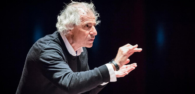 Starší muž se šedými vlasy vášnivě gestikuluje během proslovu. Nosí tmavě šedý svetr a vypadá zapáleně. | © Franois Volpe