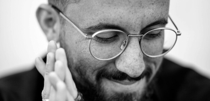 Ein lächelnder Mann mit Brille, der seine Hände zusammengelegt hat. Er trägt ein schwarzes Oberteil und hat einen Bart. | © Felix Broede_Sony Classical