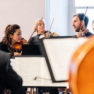 An ensemble is performing in a bright room. The musicians are playing different instruments and are focused on the performance. | © Ebihara Photography