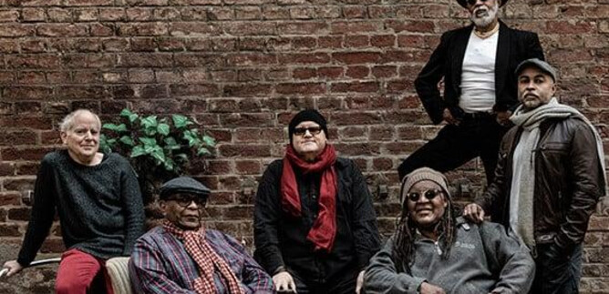 Un grupo de seis hombres está sentado y de pie frente a una pared de ladrillos. Llevan ropa diferente y posan de manera relajada en la escena. | © Jan Scheffner