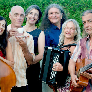 Un grupo de seis músicos está junto y sonríe a la cámara. Sostienen diferentes instrumentos y una taza en la mano. | © MÉLANGE