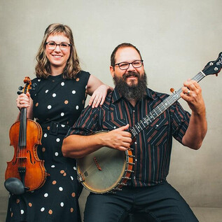 Un homme et une femme posent ensemble avec des instruments. La femme tient un violon et l'homme joue du banjo, tous deux sourient à la caméra. | © Sandlin Gaither