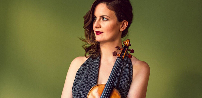 A woman is holding a violin and is gazing thoughtfully into the distance. The background is a soft green. | © Louie Thain