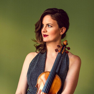 A woman is holding a violin and is gazing thoughtfully into the distance. The background is a soft green. | © Louie Thain