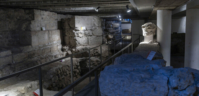 Eine archäologische Ausgrabungsstätte mit alten Steinen und Mauern. Es gibt eine Metallbrücke und beleuchtete Bereiche zur Erkundung. | © Herbert Rohrer