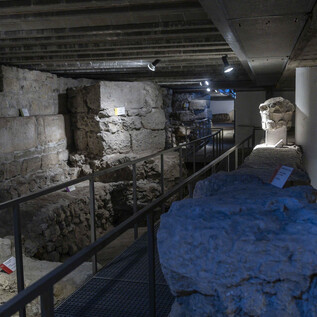 Un site archéologique avec des pierres et des murs anciens. Il y a un pont en métal et des zones éclairées pour l'exploration. | © Herbert Rohrer