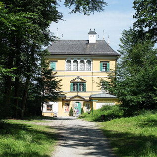 Ein großes, gelbes Haus umgeben von grünen Bäumen. Der Weg führt direkt zum Eingang des Gebäudes. | © Salzburg Museum