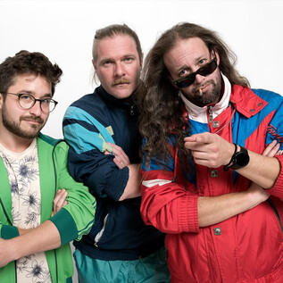 Három férfi színes sportdzsekikben együtt pózol. Különböző kiegészítőik és arckifejezéseik vannak, amelyek laza és magabiztos benyomást keltenek. | © Prenninger