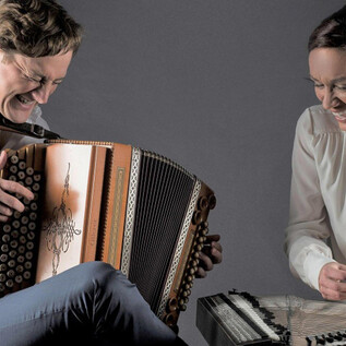 A man is playing the accordion while a woman sits at another musical instrument. Both appear to enjoy the music. | © Foto Flausen
