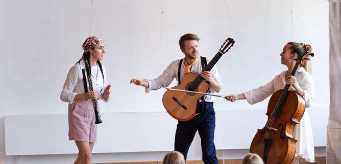 A lively music performance with three artists on stage. The audience, predominantly children, watches attentively. | © Jakob Schad
