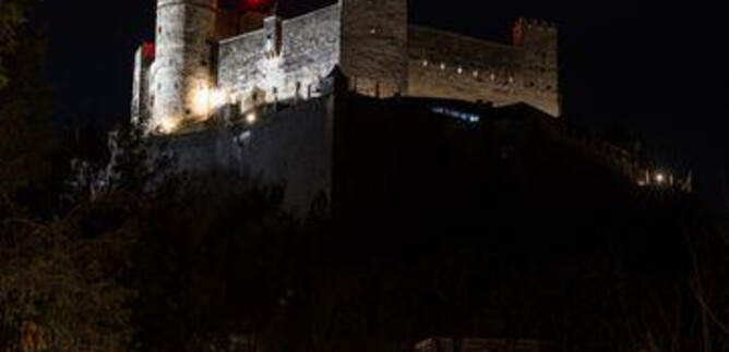 A creepy carved pumpkin glows in front of an old castle at night. The atmosphere is mysterious and fitting for Halloween. | © Festung Hohensalzburg