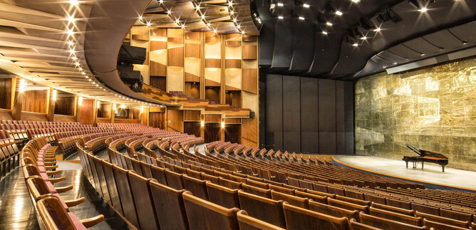 Ein Dirigent leitet ein Orchester auf der Bühne. Die Zuschauer im Hintergrund sind aufmerksam und genießen die Aufführung. | © Salzburger Festspiele / Andreas Kolarik