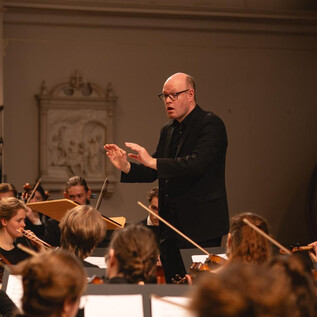 Una actuación musical en una iglesia decorada festivamente. Cuatro músicos tocan ante un público, rodeados de abetos y luces de colores. | © Simone Both
