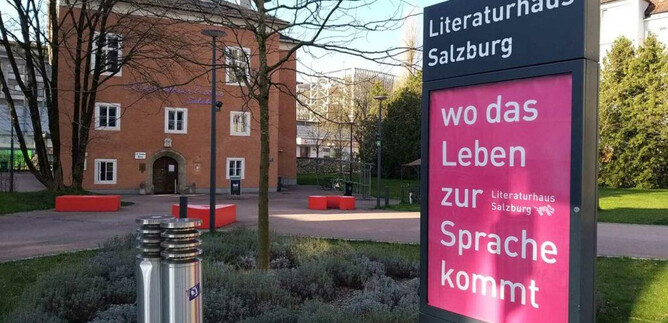 Das Literaturhaus Salzburg ist ein modernes Gebäude mit einem einladenden Außengelände. Neben dem Hauptbüro steht ein Informationsschild mit dem Spruch "wo das Leben zur Sprache kommt". | © Literaturhaus Salzburg