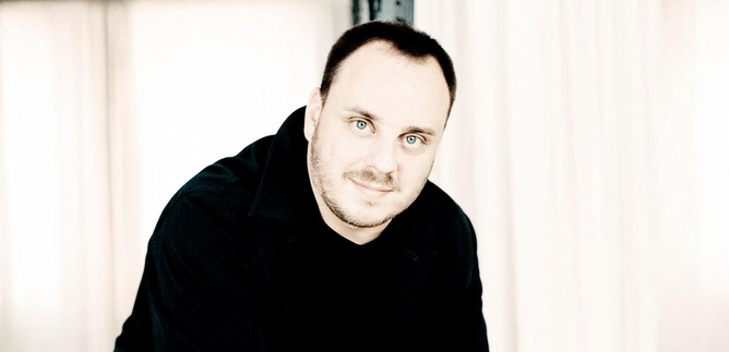 A man with short hair stands in a bright room. He has a friendly expression and is wearing a black top. | © Marco Borggreve