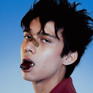 Mladík s rozcuchanými vlasy se dívá přímo do kamery. Má náplast na nose a výrazný výraz v obličeji. | © Mala Kolumna