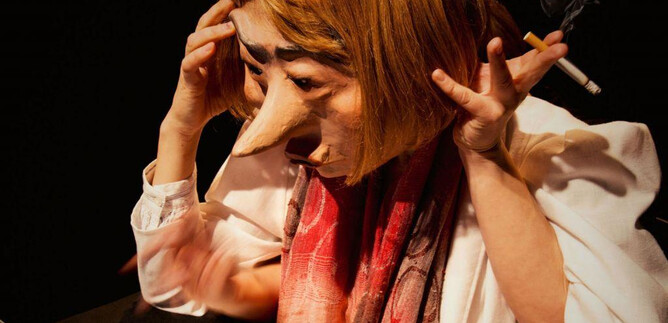 Eine Person mit einer großen Maske sitzt vor einem Laptop. Sie sieht gestresst aus und hält eine Zigarette in der Hand. | © Debra Tchotchov