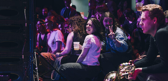 A lively event with happy people in the audience. Some are sitting and enjoying the atmosphere, while others are performing on stage. | © Michael Klimt