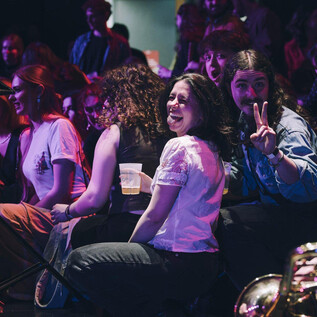 A lively event with happy people in the audience. Some are sitting and enjoying the atmosphere, while others are performing on stage. | © Michael Klimt