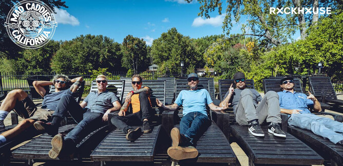 A group of seven men relaxes on lounge chairs outdoors. In the background, there are trees and a blue sky. | © Mad Caddies