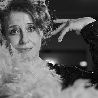 Žena s péřovou šálou elegantně pózuje. Nosí třpytivý černý outfit a má okouzlující aurou. | © Martina Bogdahn