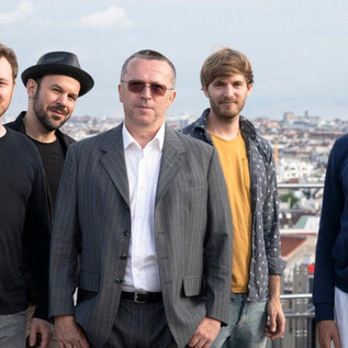 A group of five men stands against an urban backdrop. They are smiling and wearing various relaxed clothing styles. | © Hans Klestorfer