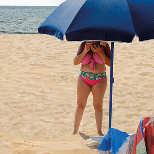 Une personne se tient sur la plage sous un parasol. Le sable est clair et la mer est visible en arrière-plan. | © Valentina Schuster