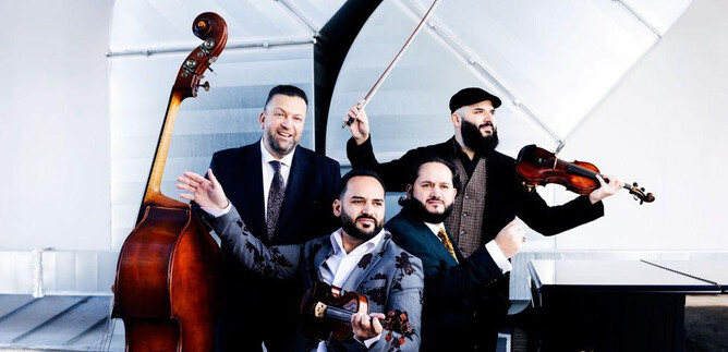 Un gruppo di quattro musicisti che suonano vari strumenti, tra cui un contrabbasso e un violino. Indossano abiti eleganti e posano insieme in un ambiente moderno. | © Julia Wesely