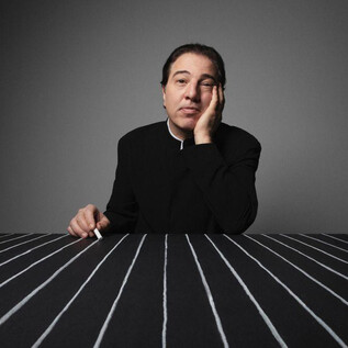 Un homme pensif est assis à une table avec des rayures noires et blanches.  
Il a une main sur son visage et a l'air sérieux. | © Fethi Karaduman