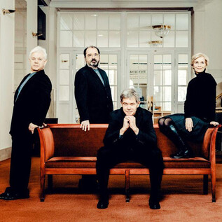 A four-person group of people stands and sits on a sofa in a modern interior. All are dressed in black clothing and are looking at the camera. | © Andrej Grilc