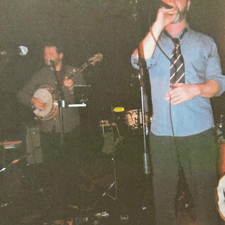 Zespół gra na żywo na scenie. Wokalista stoi na pierwszym planie, a inni muzycy grają na różnych instrumentach w tle. | © Jazzit