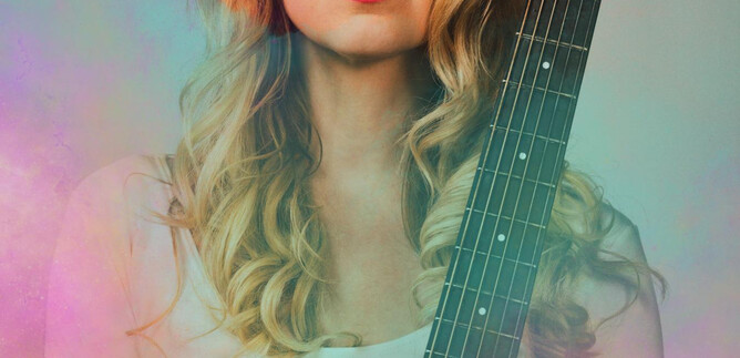 A young woman with blonde curls holds an acoustic guitar. She has a confident smile and is wearing a simple top. | © Christian Verch