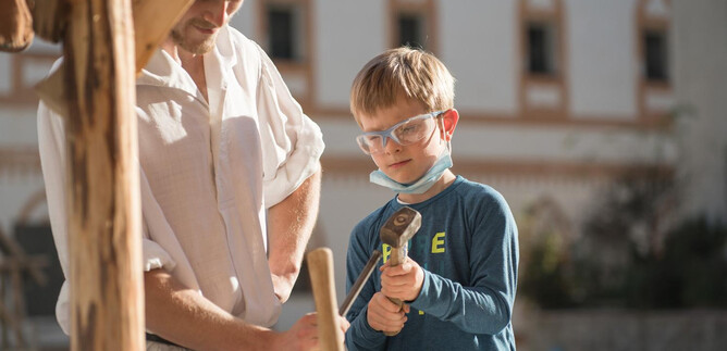 An adult and a child are working together on a rock block. The child is wearing safety glasses and holding a hammer in their hand. | © Salzburger Burgen & Schlösser