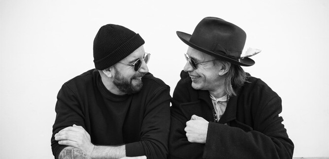 Zwei Männer lachen und blicken sich freundlich an. Sie tragen Sonnenbrillen und stylische Hüte. | © Daniela Matejschek