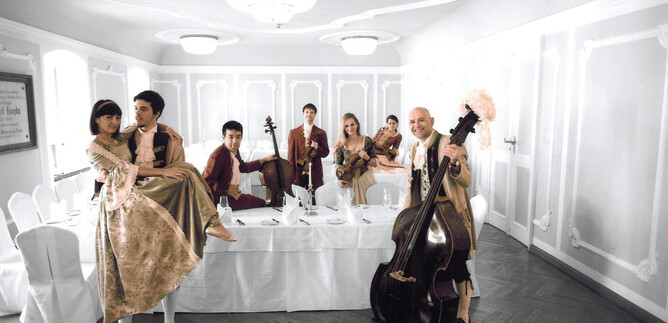 An elegant group of musicians and dancers in a festive room. They are wearing stylish clothing and posing around a set table. | © Nancy_Horowitz