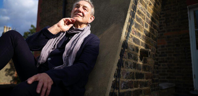 An older man is sitting relaxed on a wall and smiling. He is wearing a scarf and has a thoughtful pose. | © Gerard Collet