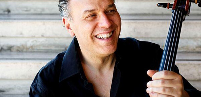 A smiling cellist sits on a staircase holding his cello. He wears a black shirt and radiates joy. | © Musacchio,-Ianniello-e-Pasqualini