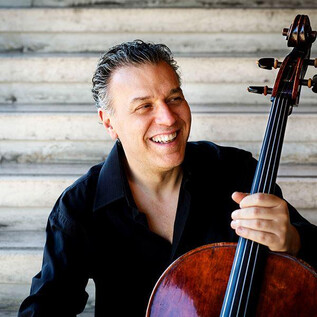 Usmívající se violoncellista sedí na schodech a drží své violoncello. Má na sobě černou košili a vyzařuje radost. | © Musacchio,-Ianniello-e-Pasqualini