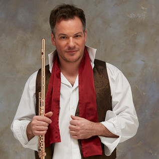 A man holds a flute in his hand and wears an elegant outfit with a red scarf. The background is neutral and slightly textured. | © Fabien Monthubert