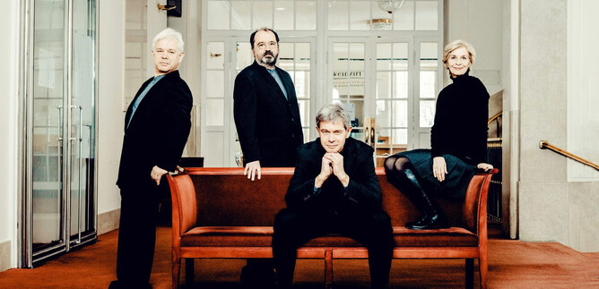 A group of four people is standing and sitting on a sofa in a bright interior. They are all wearing black clothing and looking at the camera. | © Andrej Grilc