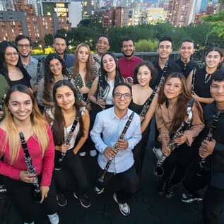 A group of young musicians stands together holding clarinets. In the background, city buildings and trees are visible. | © Daniel Romero_Iberacademy