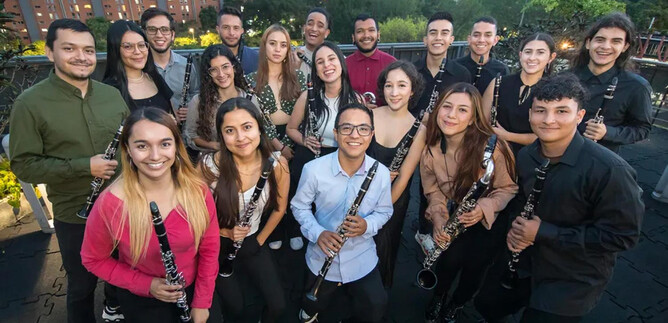 A group of young musicians stands together smiling, all holding clarinets in their hands. In the background, skyscrapers and trees can be seen under a clear evening sky. | © Daniel Romero_Iberacademy
