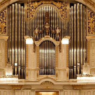 An impressive organ with golden decorations in a festive room. The walls are brightly and elegantly designed, featuring hanging lights. | © Wolfgang Lienbacher