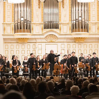 An orchestra on stage with a variety of musicians and instruments. In the background, one can see an impressive organ and an audience that is applauding. | © Wolfgang Lienbacher