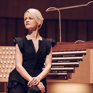 A woman sits at an organ and gazes thoughtfully into the distance. The organ has a modern design with many keys and knobs. | © Ko Cheng Lin