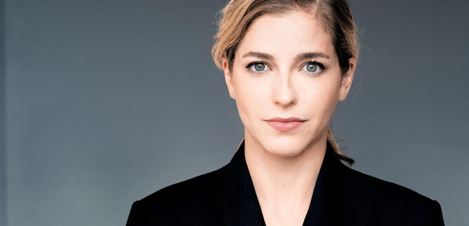A person with blonde hair and a serious expression looks directly at the camera. They are wearing a black jacket against a neutral background. | © Mathias Bothor