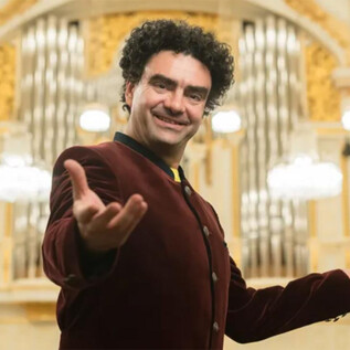 Ein Mann in einem eleganten roten Jackett steht vor einer beeindruckenden Orgel in einem festlichen Saal. Er lächelt und scheint das Publikum willkommen zu heißen. | © Wolfgang Lienbacher